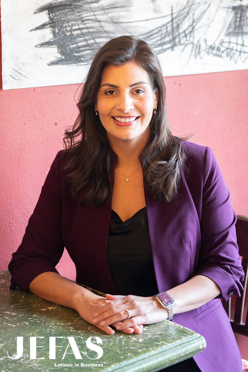 businesswoman Miriam De Dios faces camera in purple blazer over black dress, seated at a table.
