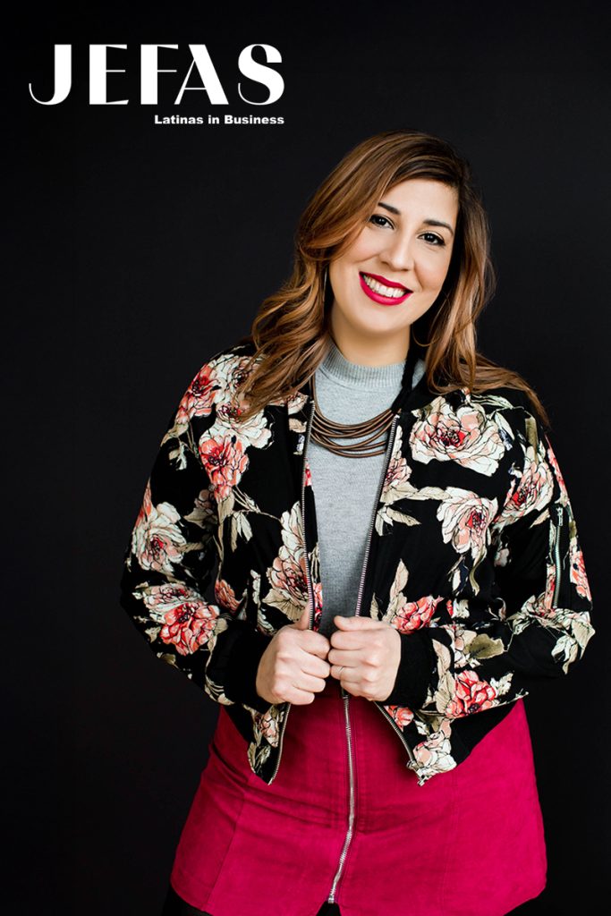 Woman looks at camera while holding jacket in front of black background.